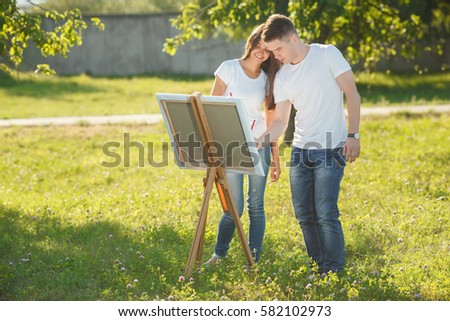Young couple drawing at easel by colorful variegated paints. Pretty young woman and handsome guy having fun with paints outdoors.