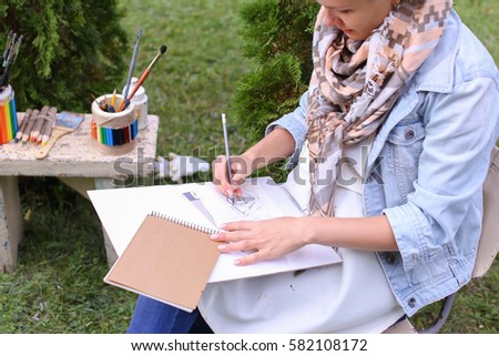 Contemporary Artist Works on Facial Contour of Depicted on Portrait Unknown Girl, Draws Sketch of Fictional Head, Prepares Gift For Friend. Woman Located in Park Outdoors in Background Stands Bench