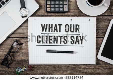 What Our Clients Say statement on paper note pad. Office desk with electronic devices and computer, wood table from above, concept image for blog title or header image. Aged vintage color look. Royalty-Free Stock Photo #582114754