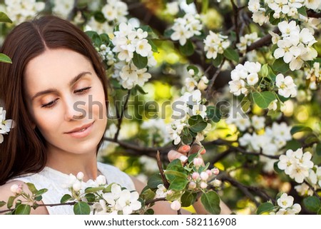 Young attractive girl with straight long hair standing in flowering Apple orchards. Beauty smiling woman looking at white flower 