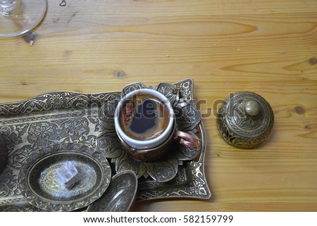 Traditional spicy turkish coffee in a small white cup with pepper and a copper serving set