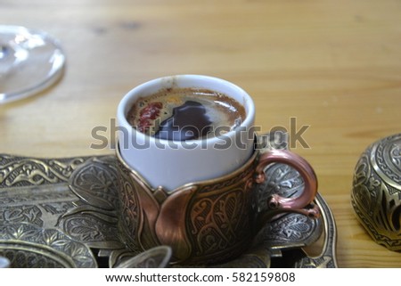 Traditional spicy turkish coffee in a small white cup with pepper and a copper serving set