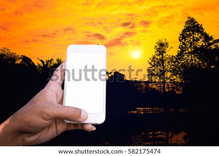 Person is taking photo a sunset above the river with a smartphone.