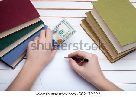 On a wooden table hardcover books and the sheet of paper on which in hands the ink handle and write.