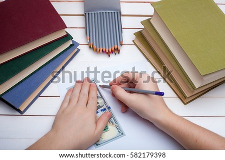 On a wooden table hardcover books with a pencil and the sheet of paper on which in hands the pencil draw.