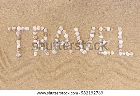 Travel written with seashells on a sand beach.