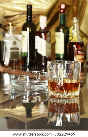 Glass of cognac, brandy or whiscy on mirror table. bottles in a bar on the background.