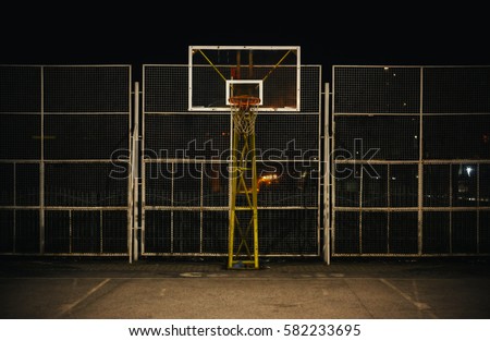 The basketball court during night, view on basketball hoop and fence.