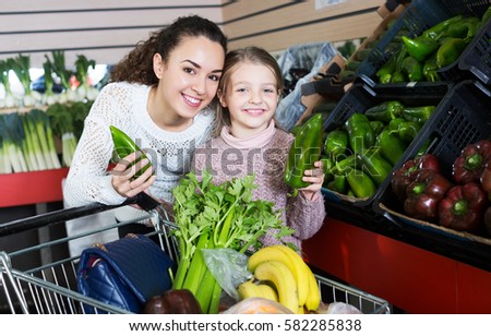 Portrait of young mother with little girl purchasing shallot and celery