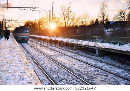 Photo of bright and beautiful sunset on a cloudy sky in cold winter season. Railway track with platforms for waiting trains and power transmission lines in the middle of winter forest landscape