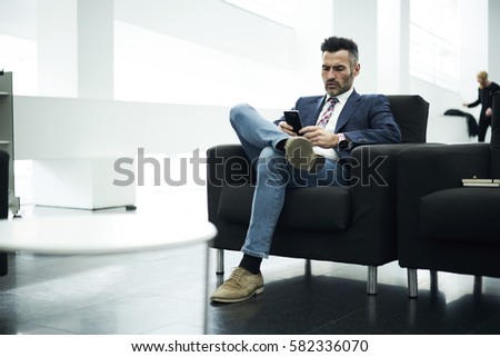 Skilled well-dressed businessman waiting for meeting with partners  while making online payments on finance banking service using application on smartphone connected to free wireless internet