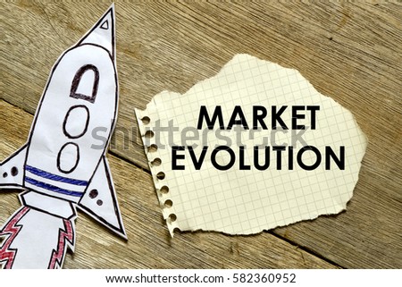 Paper rocket with paper written MARKET EVOLUTION on wooden background. Business concept.