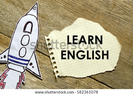 Paper rocket with paper written LEARN ENGLISH on wooden background. Business concept.