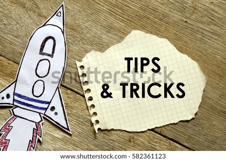 Paper rocket with paper written TIPS AND TRICKS on wooden background. Business concept