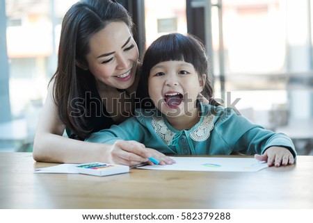 Pretty little girl with her mother painting picture at home. girl with her mom painting picture by colorful chalks at the table. Childhood and togetherness concept.