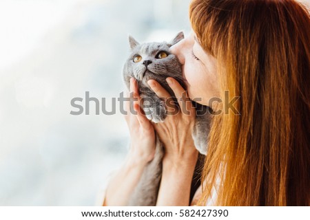 Close up of lovely middle-aged redhead woman kissing gray cat.  Royalty-Free Stock Photo #582427390