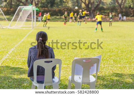 woman watching a school boy soccer game on a sunny day Royalty-Free Stock Photo #582428800