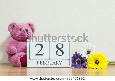 Closeup surface white wooden calendar with black 28 february word on brown wood desk and cream color wallpaper in room textured background with copy space in selective focus at the calendar