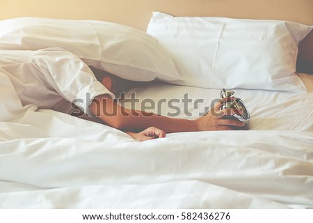 Irritated young woman putting her alarm clock off in the morning with soft morning light. Relaxing concept. Royalty-Free Stock Photo #582436276