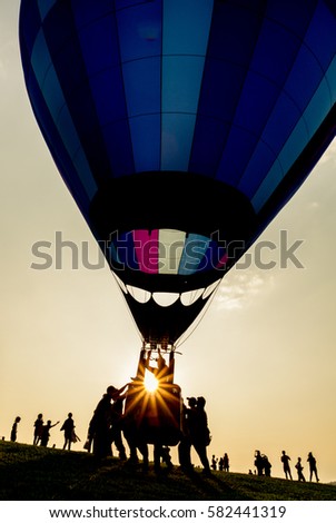 Silhouette of people with hot air balloon with colored envelope at sunset, backlit by sunlight photography