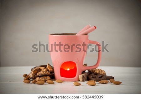 Cup fondue with candle, chocolate, cookies, almonds, romantic