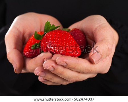 Close up picture woman holding a handful of delicious strawberries on a black background