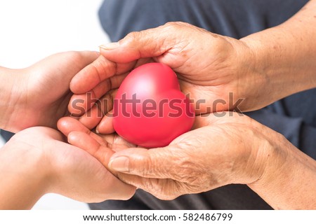 Close up of senior woman and young female hands holding red heart.National Family Caregivers Month, National Hospice Month and National Home Care Month. Age, family, love and health care concept 