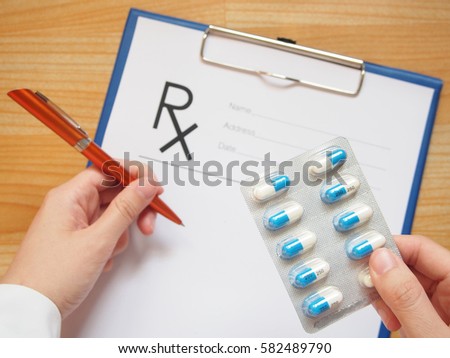 Female doctor hand holding capsule blister and writing prescription to patient at hospital or clinic. Medical treatment, antibiotics resistance problem and rational drug use concept. Selective focus. 