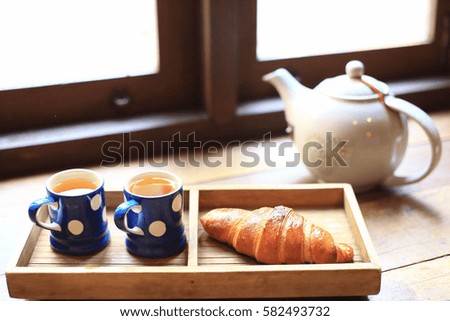The hot tea in the cups with croissants, as wood background or print card.