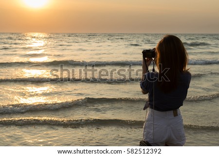 Female traveler taking a sunset photo on the beach.