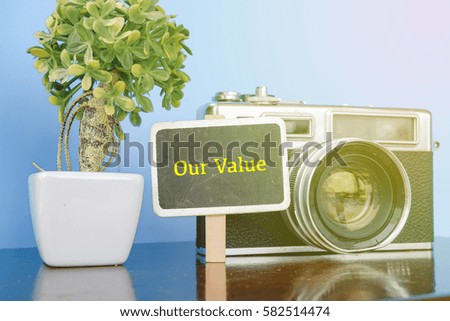 OUR VALUE word, wooden signage, vintage camera and artificial plant on wooden desk with reflection.