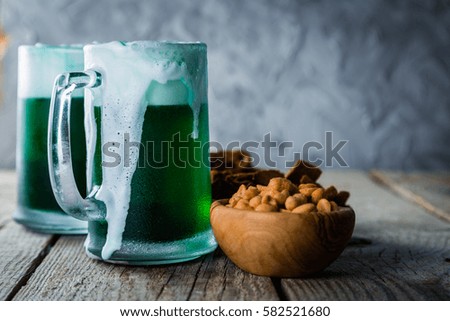 Green beer in mugs and snacks on rustic wood background, copy space