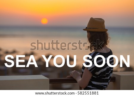 Young woman in hat and cute summer dress standing at the terrace with peaceful sea scenery, looking at sunset or sunrise on horizon, back view, copy space. Photo with motivational text "Sea you soon" 