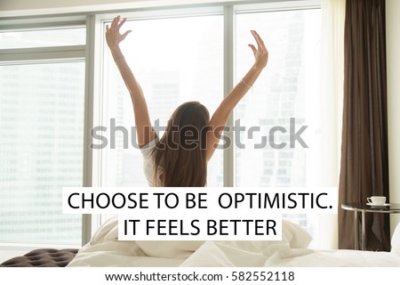 Young woman outstretching her arms sitting on bed after good night sleep, unwilling to get up and leave her comfortable nest. Photo with motivational text "Choose to be optimistic. It feels better" 