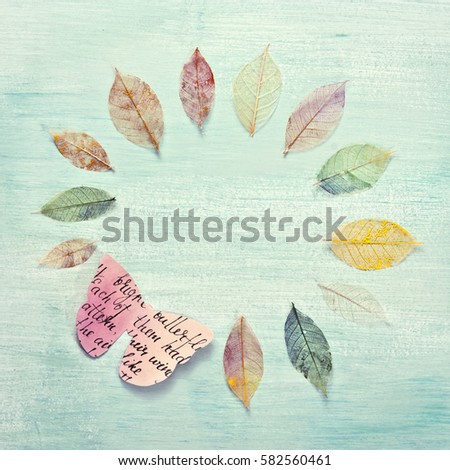 A square photo of a frame, made up by hand painted skeleton leaves and a paper butterfly on a teal background texture. A design for an autumn banner, with copyspace