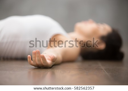Beautiful young woman working out on wooden floor, resting after doing yoga exercises, lying in Shavasana (Corpse or Dead Body Posture), relaxing. Close up, focus on hand  Royalty-Free Stock Photo #582562357