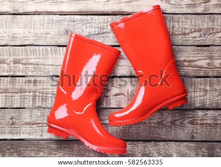 Red rubber boots on a brown wooden table Royalty-Free Stock Photo #582563335