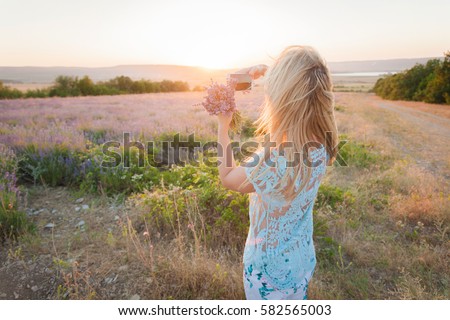 Beautiful young woman with a bouquet of lavender in a meadow makes the landscape picture on a mobile phone