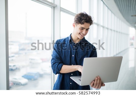 Handsome young man man holding a laptop in hall Royalty-Free Stock Photo #582574993