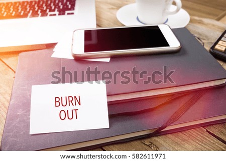 Burn Out on business card with text on office desktop with electronic devices, sun lit with lens flares.