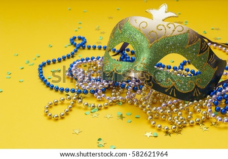 Carnival green and gold masks and beads on a yellow background. Space for text.