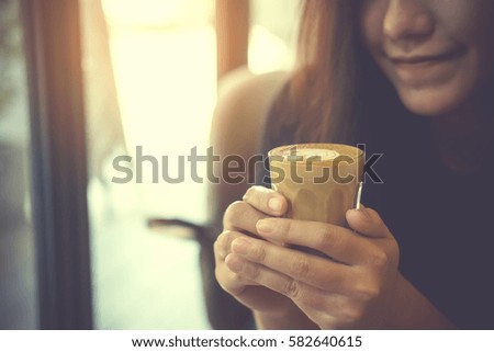 Closeup image of Asian woman holding coffee cup and smelling hot coffee with feeling good in cafe