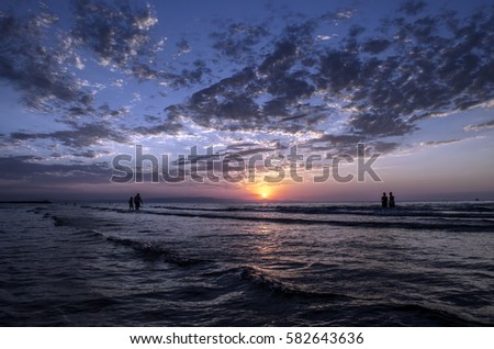 Young girls in warm water at sunset. Gorgeous colors in the sky and the sea. People standing and watching to sunset at Caspian sea. Baku, Azerbaijan. Perfect shapes reflected in water