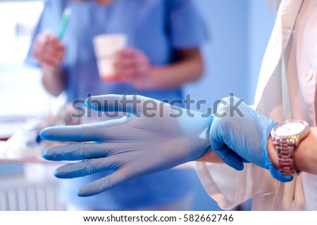 Close up of female doctor's hands putting on blue sterilized surgical gloves in the medical clinic.
