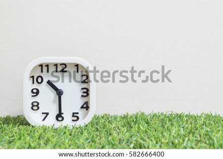 Closeup white clock for decorate show a half past ten, or 10:30 a.m. on green artificial grass floor and cream wallpaper textured background with copy space