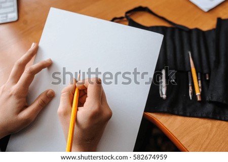 Top view of female hands with pencil on blank white paper sheet starting new picture