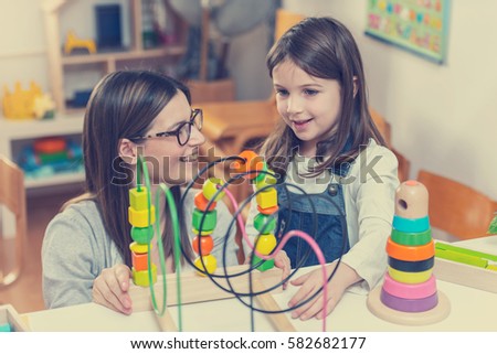 Kindergarten teacher looking at kid playing with didactic colorful toys indoors - preschool