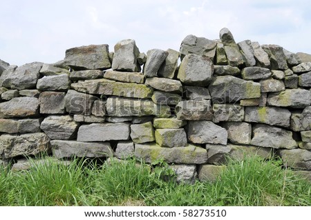 A dry stone wall made of random grey stone with grass at bottom. Royalty-Free Stock Photo #58273510