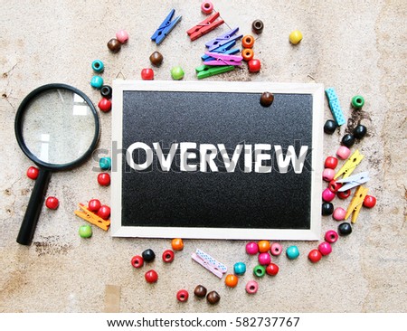 A concept image of a colorful beads and cute clothespin with a magnifying glass over a brown texture background with a chalkboard and a word OVERVIEW