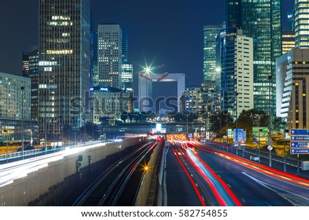 Paris cityscape with modern buildings in business district La Defense with dynamic street traffic and car lights by night. Glass facade skyscrapers. Concept of economics, finances. Copy space. Toned